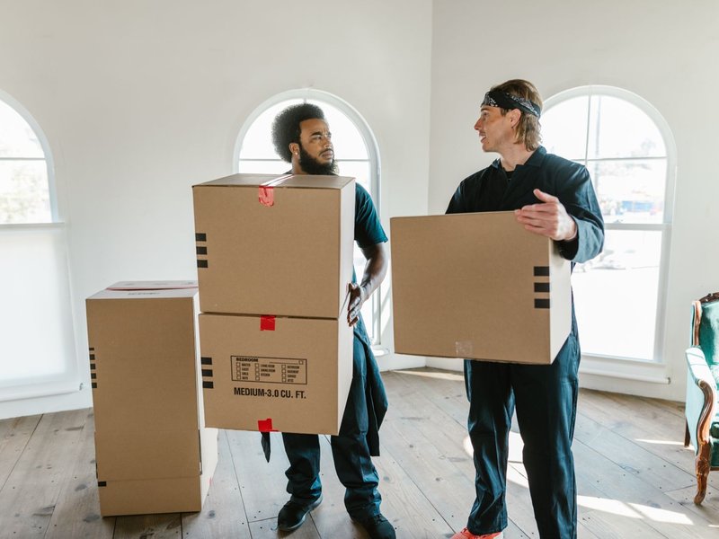 Umzugsteam trägt gestapelte Umzugskartons durch eine leergeräumte Wohnung